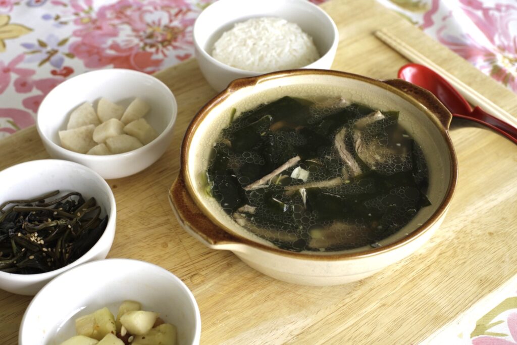 A bowl of soup made with seaweed, surrounded by four smaller bowls of rice and vegetables.