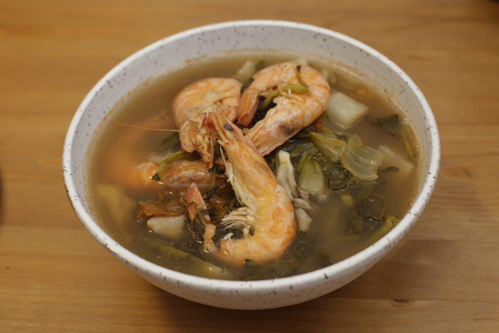 A bowl of soup with shrimp and vegetables.