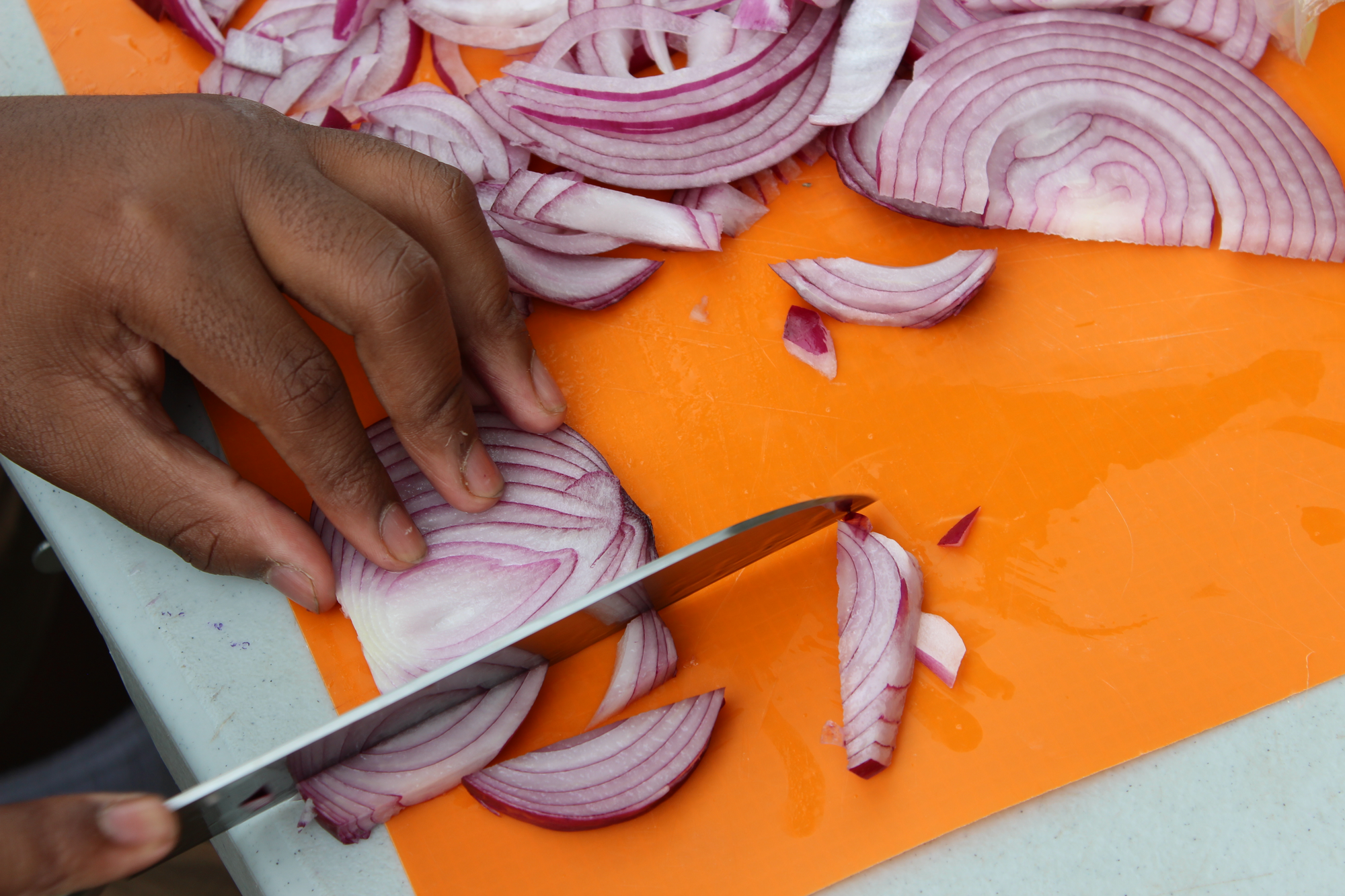 A close-up of a student's hand chopping a red onion on an orange cutting board. Massachusetts is one of many states making greater commitments to food education and nourishing school meals through food policy.