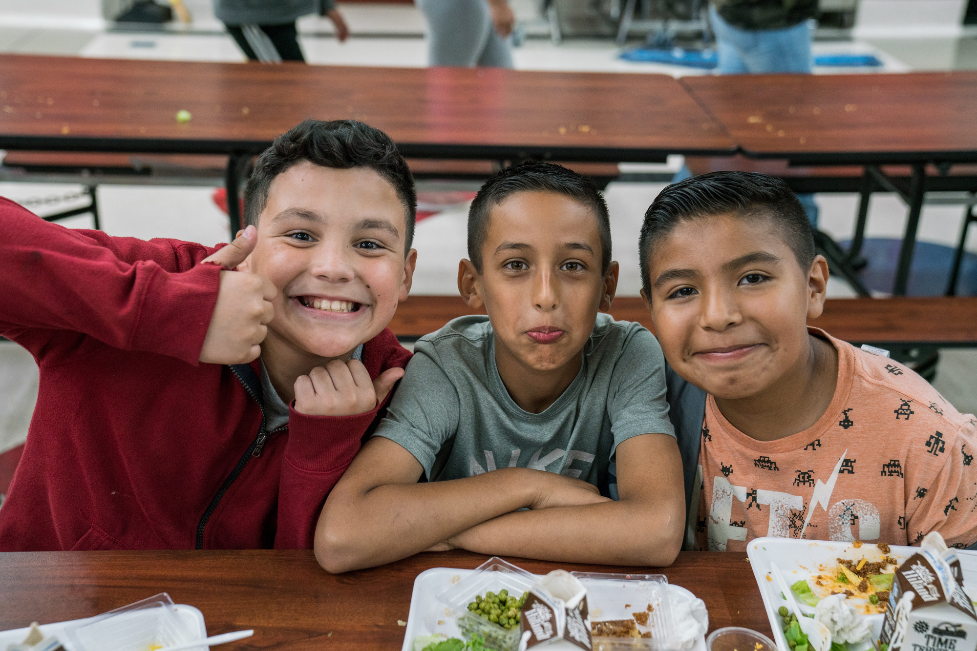 Three students sit smiling at a lunch table, trays in front of them.