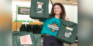 FoodCorps member Eva Gertz holds up green tote bags ready for fruit and veggie distribution. Eva shares a day in the life of a school nutrition member here.