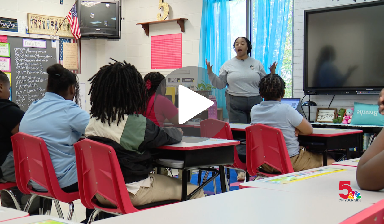 FoodCorps member Xena Wiley stands in front of a classroom full of students, wearing a grey FoodCorps sweatshirt. 