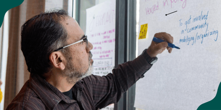 A person with short hair and glasses writes on a piece of flip chart paper about the importance of community organizing. Talking to your school board is a powerful way to uplift issues you care about.
