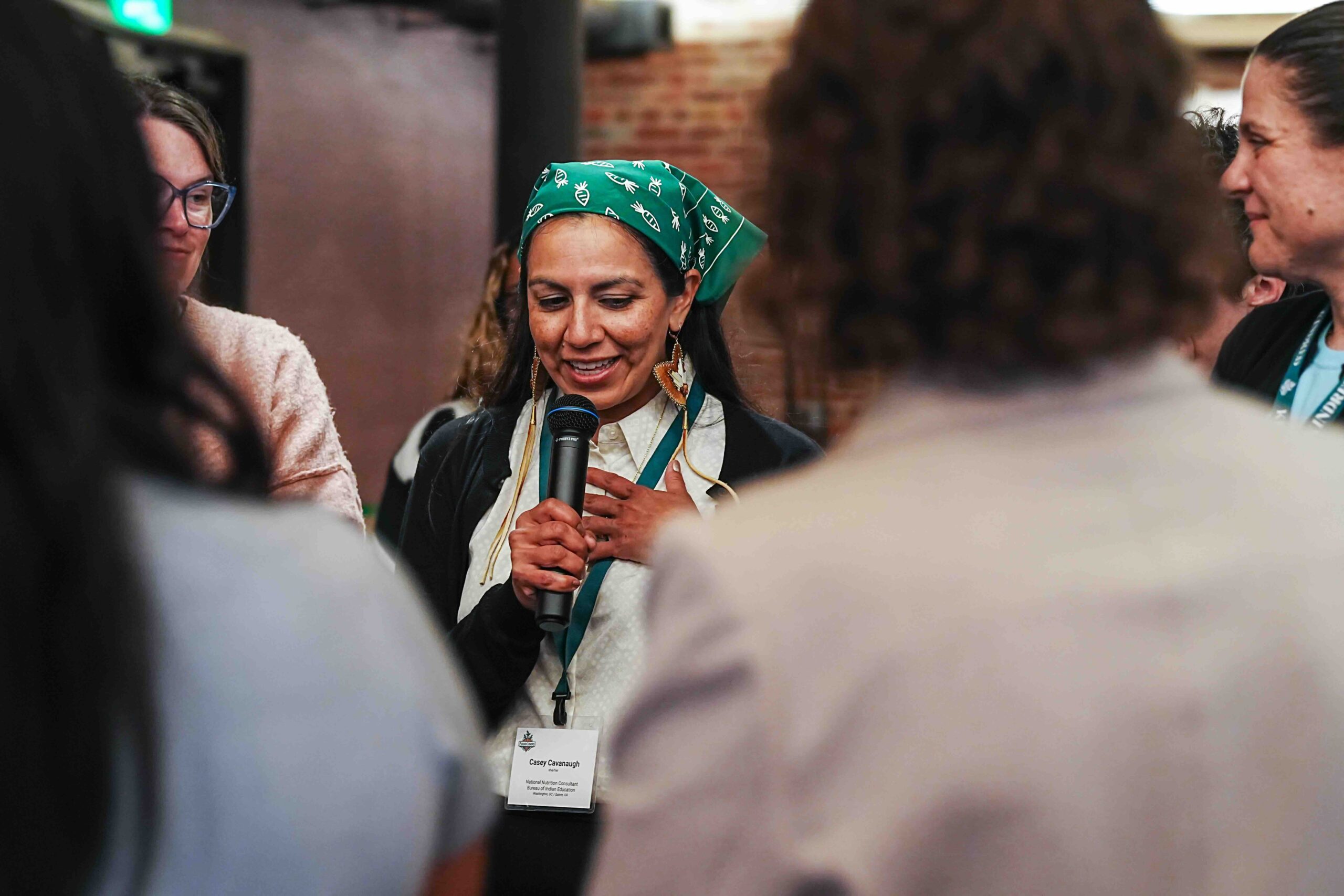 Casey Cavanaugh speaks into a microphone at the Kindred Convening in June 2026